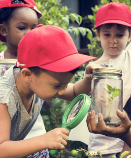 students wearing red hats using a magnify glass to look in a jar